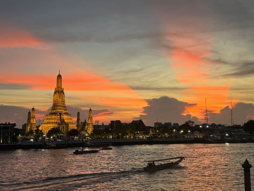 An illuminated riverside temple beneath a vivid orange sunset